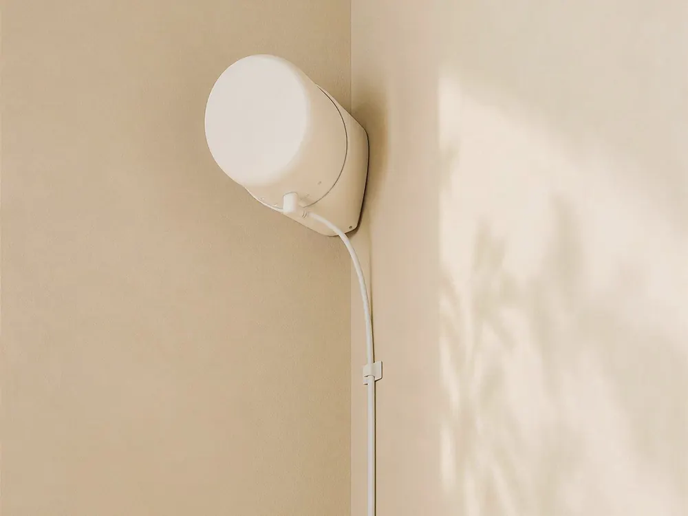 The Silvie sensor, a white cylinder on a wedge bracket, mounted where two walls meet with its cable clipped down the wall