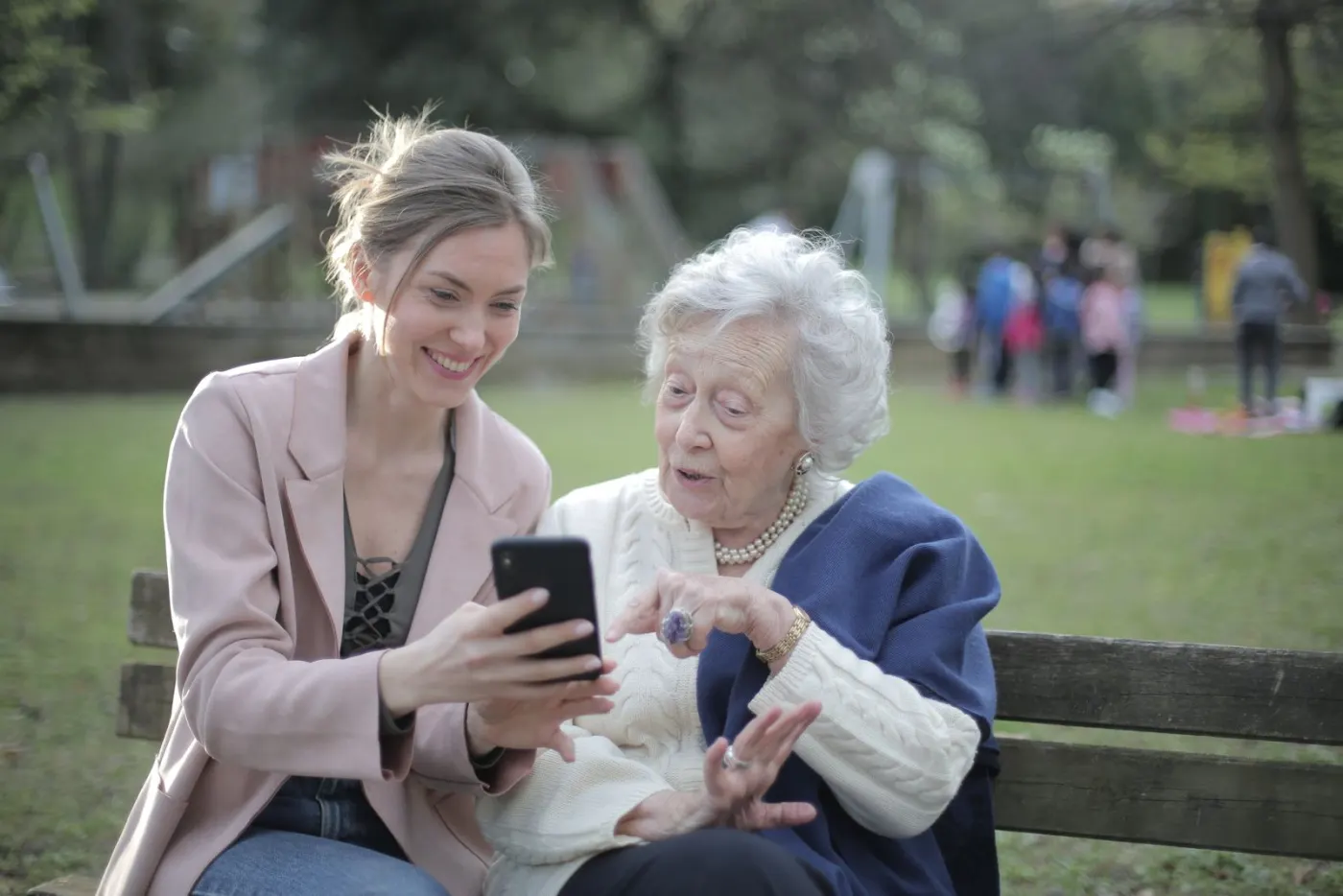 A vital senior mother and her adult daughter looking at a phone together, both engaged