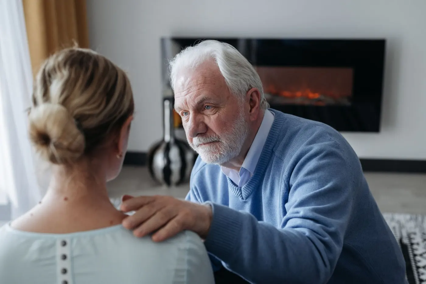 A senior father resting a hand on his adult daughter's shoulder during a tender, serious talk