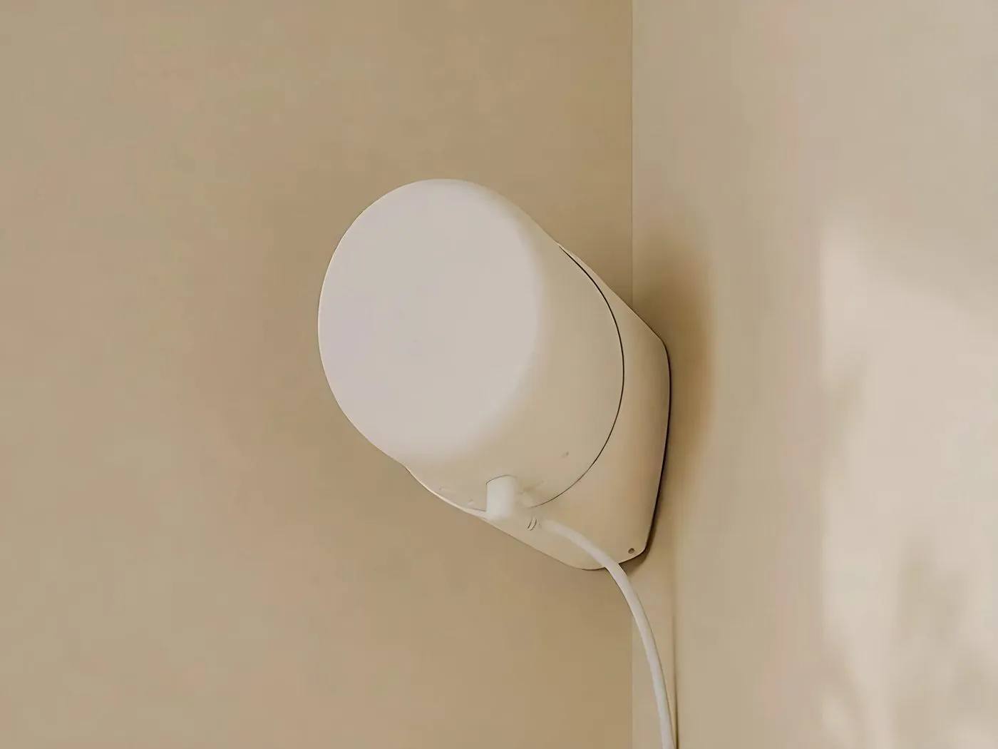 The Silvie sensor mounted in the corner of a room, plugged in with a white cable